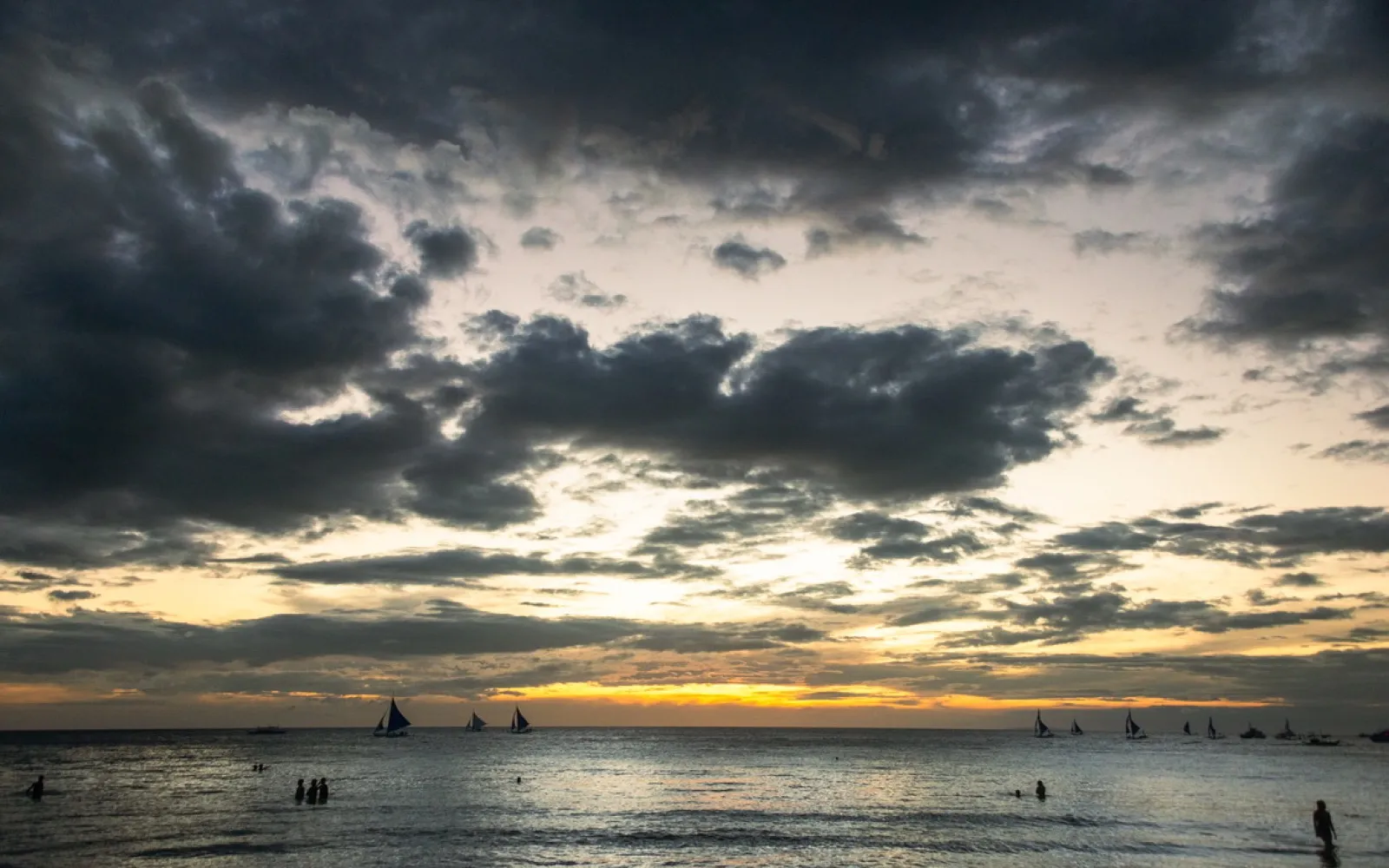 Multiple sailboats silhouetted against orange sunset